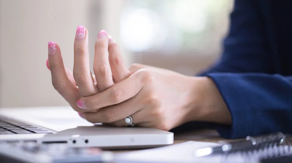 A woman holding her hand and wrist beside a laptop