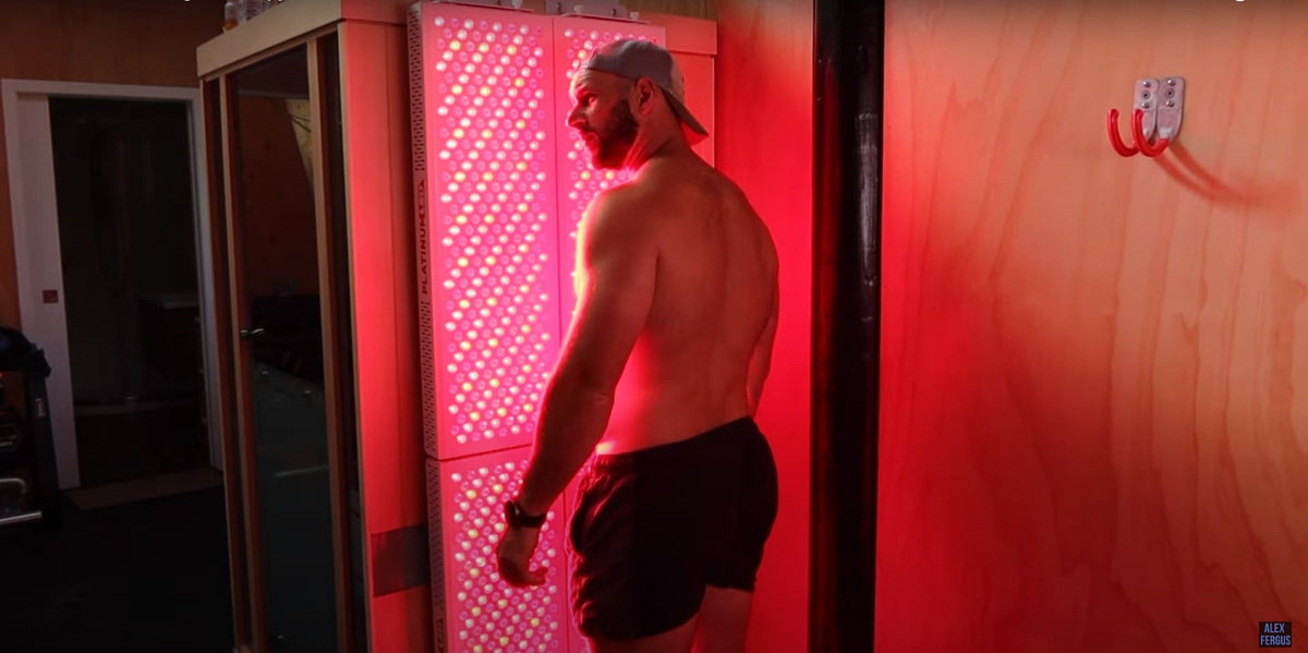An adult standing beside illuminated red light panels in a wood-paneled room.