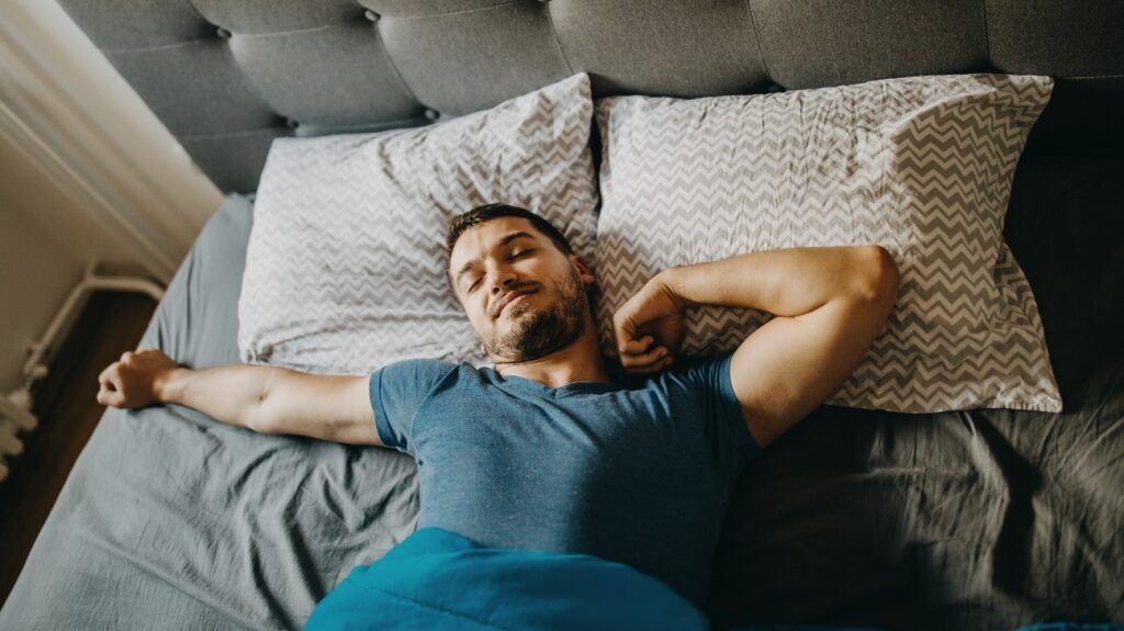 A person resting on pillows beneath a blanket in a bedroom.
