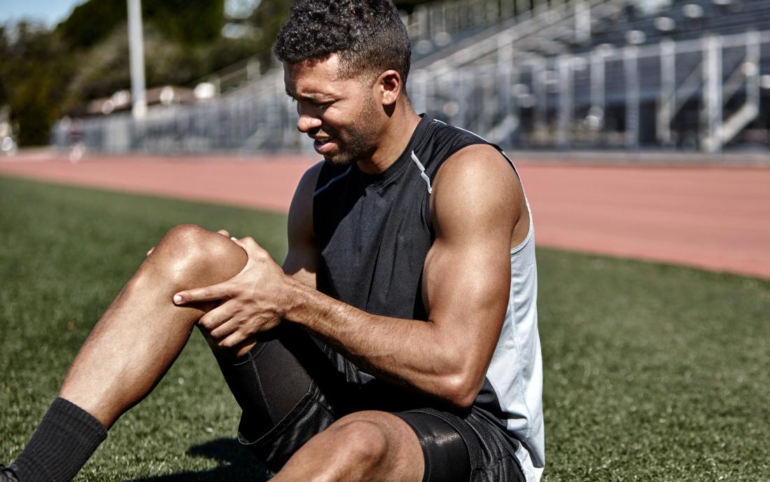 A runner seated on grass and holding the area above his knee
