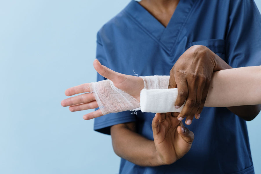 The hands of a person in blue scrubs wrapping a white bandage around another person's hand.