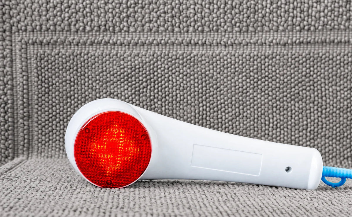 A handheld red-light device resting on a woven surface.