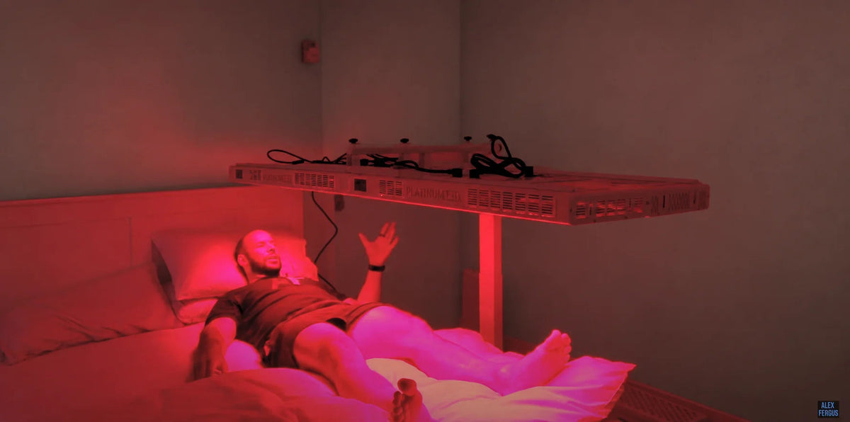 An adult reclining beneath a horizontal red light panel at home.