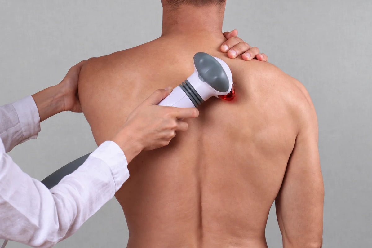 A handheld treatment instrument applied near an adult shoulder.