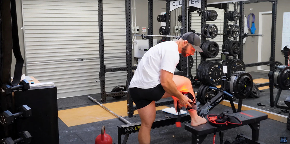 An adult fitting a red-light wrap around the lower leg in a gym.