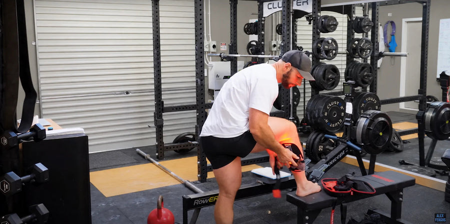 An adult fitting a red-light wrap around the lower leg in a gym.