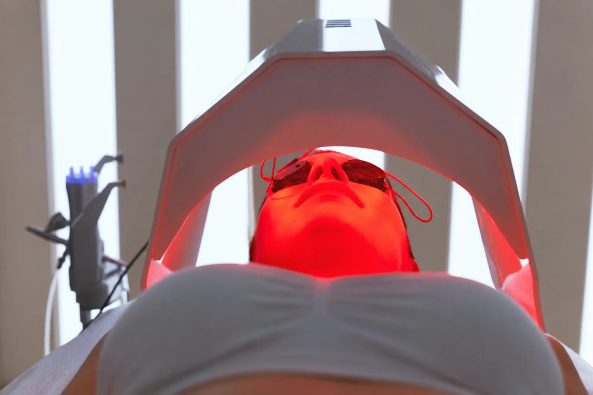 A reclining adult wearing eye protection beneath a light-treatment hood.